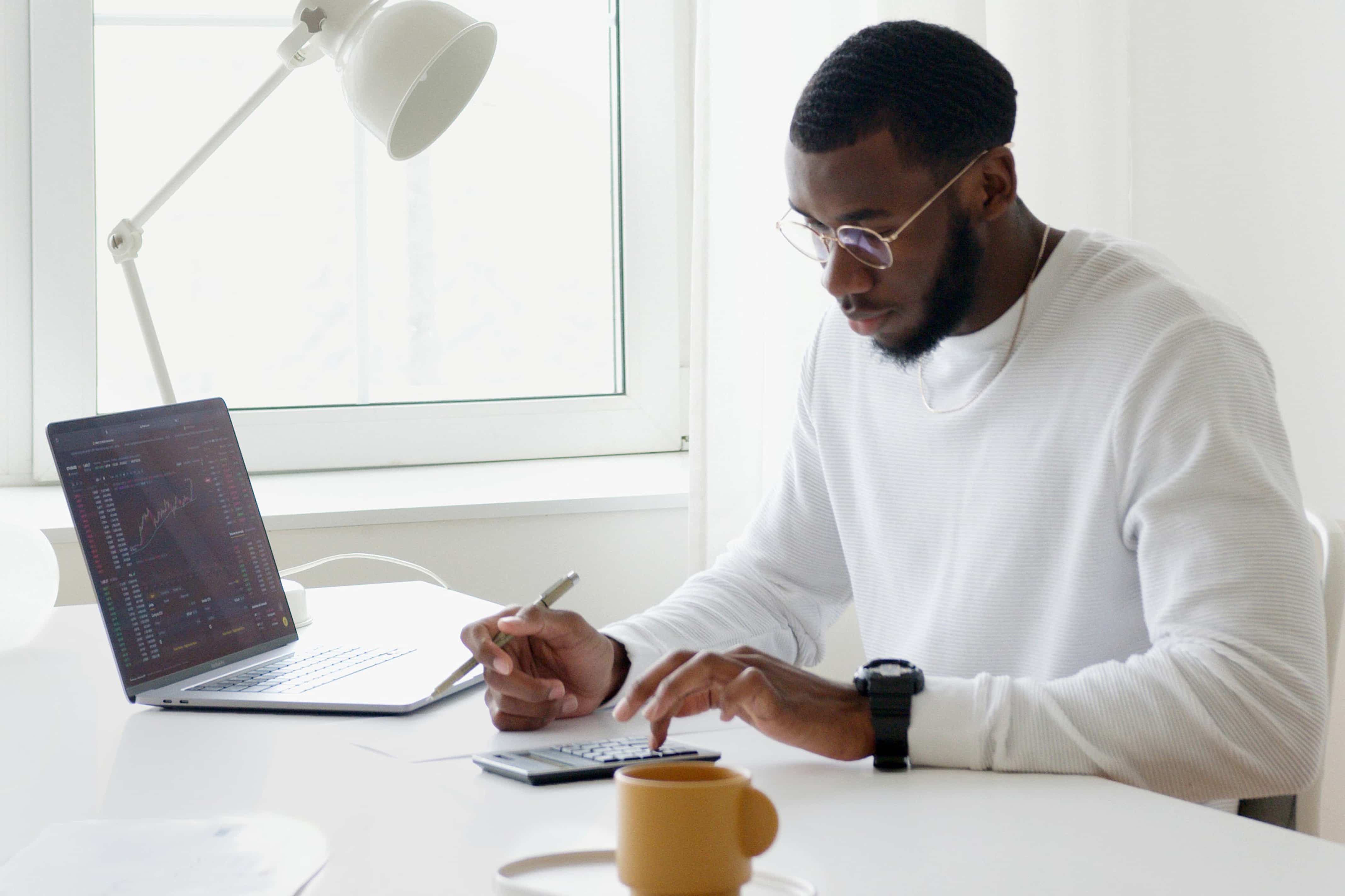 Man using a calculator with a laptop open